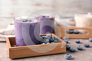 Glass of tasty blueberry smoothie and frozen berries in wooden box on table