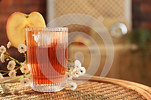 Glass of tasty cider and flowers on wicker table in room, space for text. Relax at home