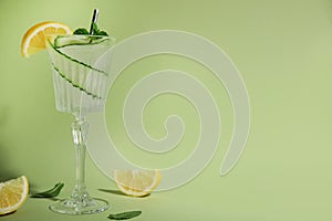 Glass of tasty fresh cucumber water with mint and sliced lemon on light green background, space for text