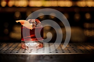 Glass of tasty fresh and strong whiskey cocktail decorated with orange peel on bar counter