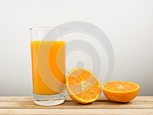 The glass of tasty pure orange juice and fresh orange half on wooden tray