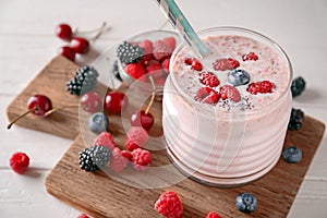 Glass with tasty raspberry smoothie and berries on light table