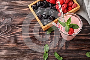 Glass with tasty raspberry smoothie and berries on wooden table