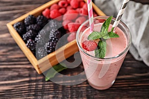 Glass with tasty raspberry smoothie and berries on wooden table