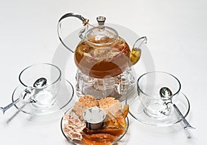 Glass tea pot with cups and crystalized fruits on white background