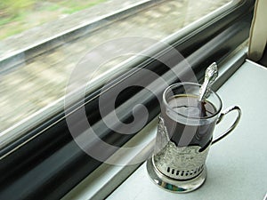 A glass of tea in a silver Cup holder is on the table in the train in front of the window.