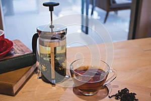 A glass of tea with tea pot on table.