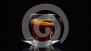 In a glass teacup of tea with tea leaves omit the sliced circle of lemon, coarsely on a black background