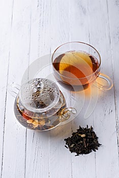 Glass teapot with blooming green tea and cup of tea on white wooden table