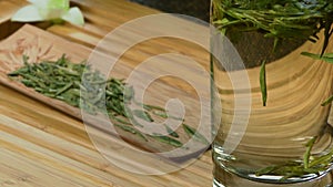 Glass teapot with blooming tea flower inside against wooden background Chinese green tea leaves close up in traditional