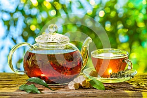 Glass teapot with brewed tea is on the table on a sunny summer day