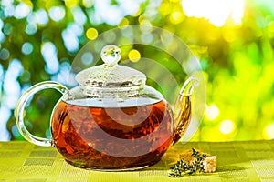 Glass teapot with brewed tea is on the table on a sunny summer day