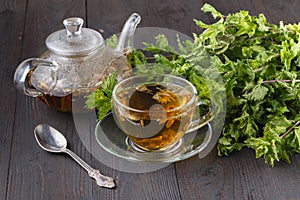 Glass teapot and cup with green tea on old wooden table with fresh herbs