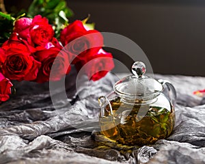 Glass teapot on a dark background. Red Roses nearby