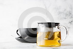 Glass teapot with dark cup of green, camomile, chamomile or yellow tea isolated on bright marble background. Overhead view, copy