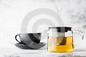 Glass teapot with dark cup of green, camomile, chamomile or yellow tea isolated on bright marble background. Overhead view, copy