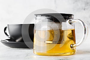 Glass teapot with dark cup of green, camomile, chamomile or yellow tea isolated on bright marble background. Overhead view, copy