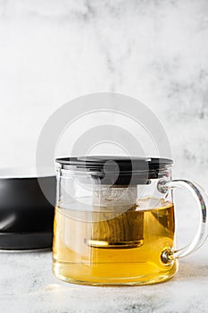 Glass teapot with dark cup of green, camomile, chamomile or yellow tea isolated on bright marble background. Overhead view, copy