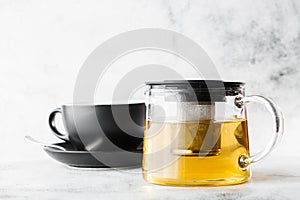 Glass teapot with dark cup of green, camomile, chamomile or yellow tea isolated on bright marble background. Overhead view, copy