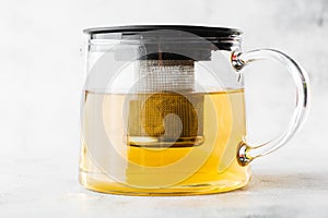 Glass teapot of green, camomile, chamomile or yellow tea isolated on bright marble background. Overhead view, copy space.