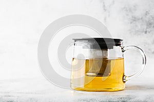 Glass teapot of green, camomile, chamomile or yellow tea isolated on bright marble background. Overhead view, copy space.