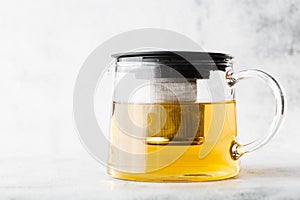 Glass teapot of green, camomile, chamomile or yellow tea isolated on bright marble background. Overhead view, copy space.