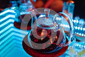 Glass teapot in the hookah room on the table with a mirror surface and neon lighting