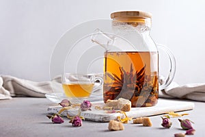Glass teapot of hot fragrant craft blossom tea with cup and dry rose bud, sugar