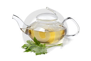 Glass teapot with lovage tea and a fresh twig of lovage on white background