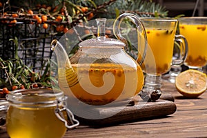 Glass teapot with orange sea buckthorn tea. Hot winter drinks on brown wooden background