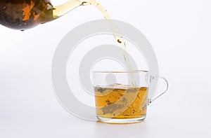 Glass teapot pouring green tea into cup isolated on white
