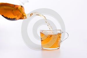 Glass teapot pouring green tea into cup isolated on white