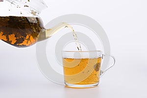 Glass teapot pouring green tea into cup isolated on white background