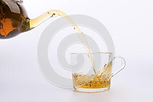 Glass teapot pouring green tea into cup isolated on white background