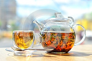 A glass teapot with tea and a cup with tea stand on the table