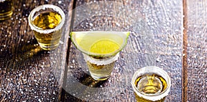Glass of tequila, on wooden table, with lemons and salt in the background. fiery drink with vodka