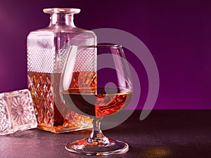 glass textured square bottle and glass goblet with amber alcohol brandy scotch whiskey. violet. Horizonal