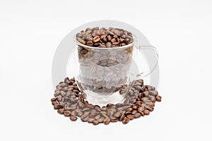 Glass thermos insulating cup transparent overfilled with roasted coffee beans on white underground