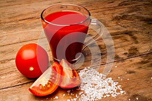 Glass with tomato juice and ripe tomatoes on a wooden table