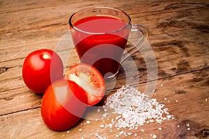 Glass with tomato juice and ripe tomatoes on a wooden table