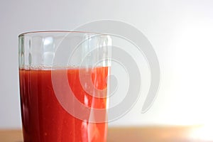 Glass of tomato juice on table on blurred background in kitchen interior. Natural lighting