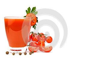 A glass of tomato juice with a tomato slice on the edge. Tomatoes, parsley and allspice are spread around