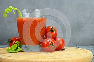 A glass of tomato juice, tomatoes, parsley leaves on a cutting board