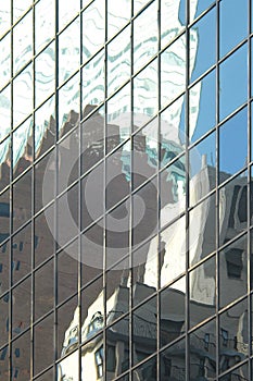 Glass tower office building exterior windows reflecting and distorting nearby  skyscrapers and blue sky in Midtown Manhattan, New