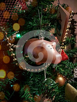 a glass toy in the form of a pink pig hangs on a decorated Christmas tree