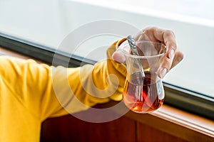 A glass of traditional turkish tea cup on traveler hand service on travel boat. Male hand holding a cup of turkish tea in the