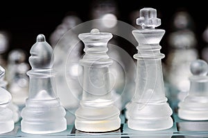 glass, transparent chess pieces on a checkerboard, selective focus, close-up, isolated on black