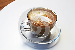 Glass transparent cup with coffee in a glass saucer on a white table