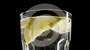 In a glass transparent glass with carbonated water floating slices of yellow lemon. Bubbles slowly rise up.