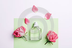 Glass transparent perfume bottle and pink rose flowers on green and white background. Top view, flat lay, mockup